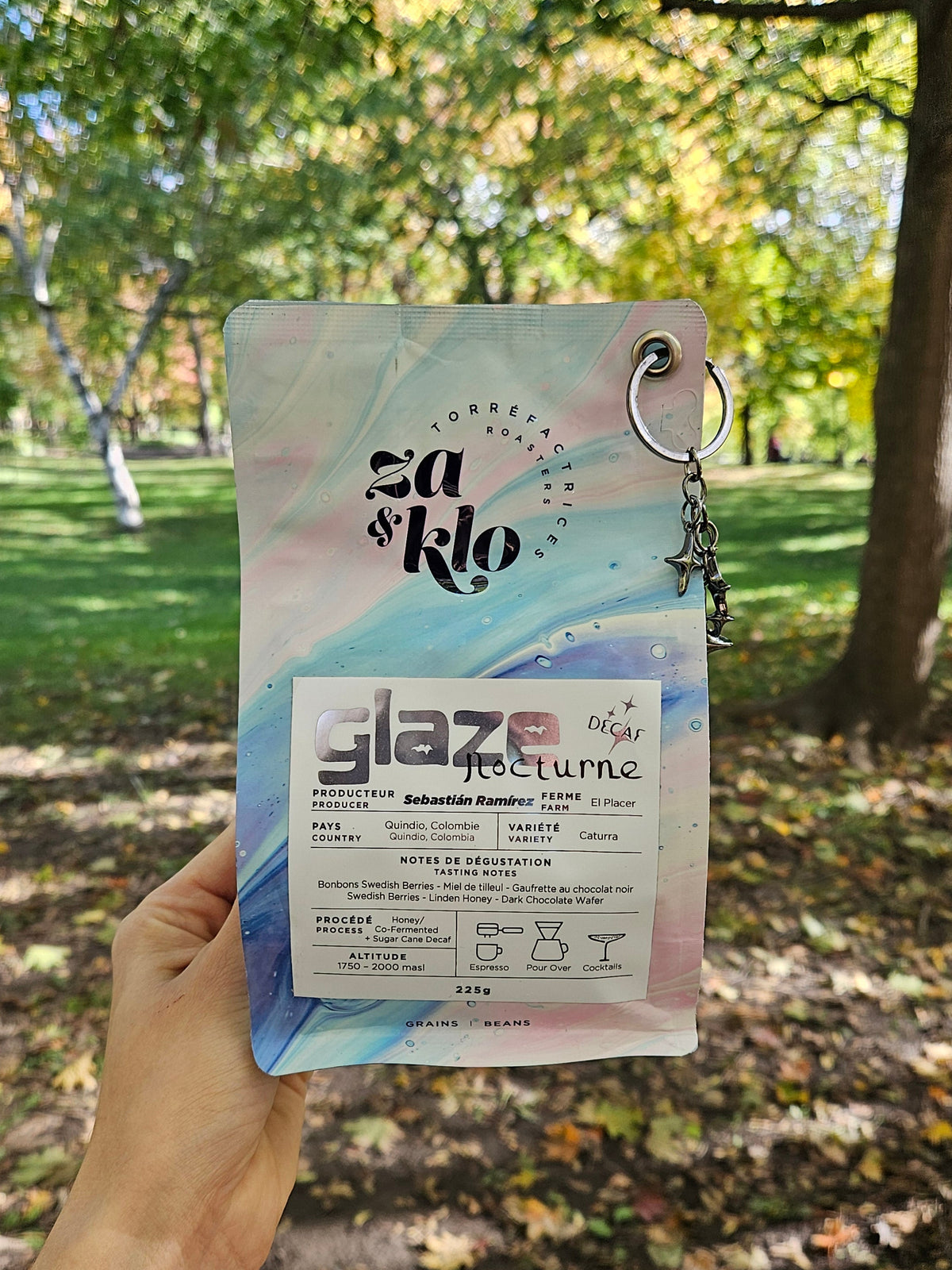 Photo of Glaze nocturne, a decaf  'honey' co-fermented coffee from Colombia produced by Sebastian Ramirez, with a star-shaped keychain attached to the bag. The bag highlights fruity notes of strawberry yogurt, cranberries, and linden, with visible typography displaying the name 'Glaze.' The 120-hour anaerobic fermentation with red wine yeast, dehydrated strawberries, and red fruits create a texture reminiscent of autumn honey. Ideal for espresso or pour-over. Roasted by Za and Klo Roastery