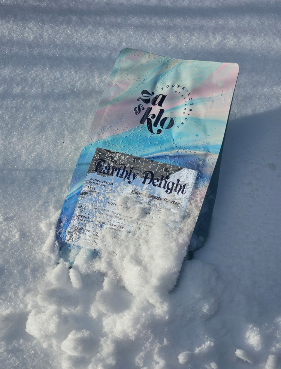 Image of Za & Klo coffee bag with reflective label, buried in snow. winter release of coffee. Coffee has notes of rose, pistachio, honey and orange blossom. Za and Klo's coffee named earthly delight.
